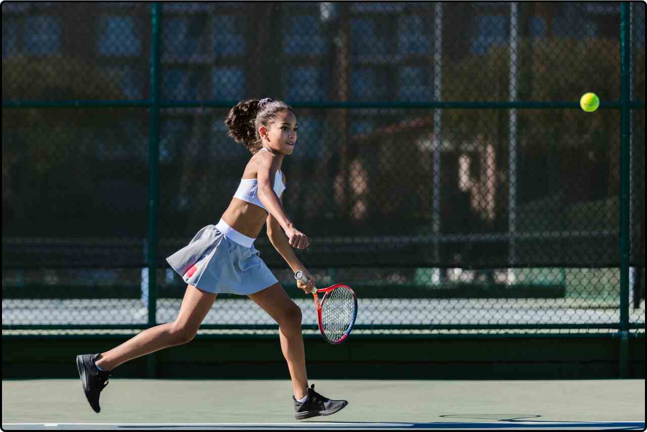 Young girl practicing tennis, hitting the ball with her racket.